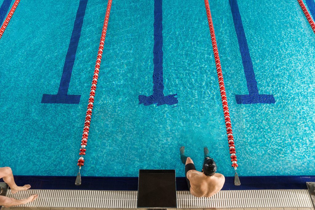 Man sitting on the edge of a pool learning to clean swim lane lines